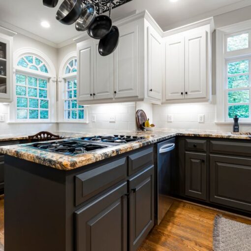 Modern kitchen with dark gray lower cabinets, white upper cabinets, a granite island with a gas stove, and a hanging pot rack.