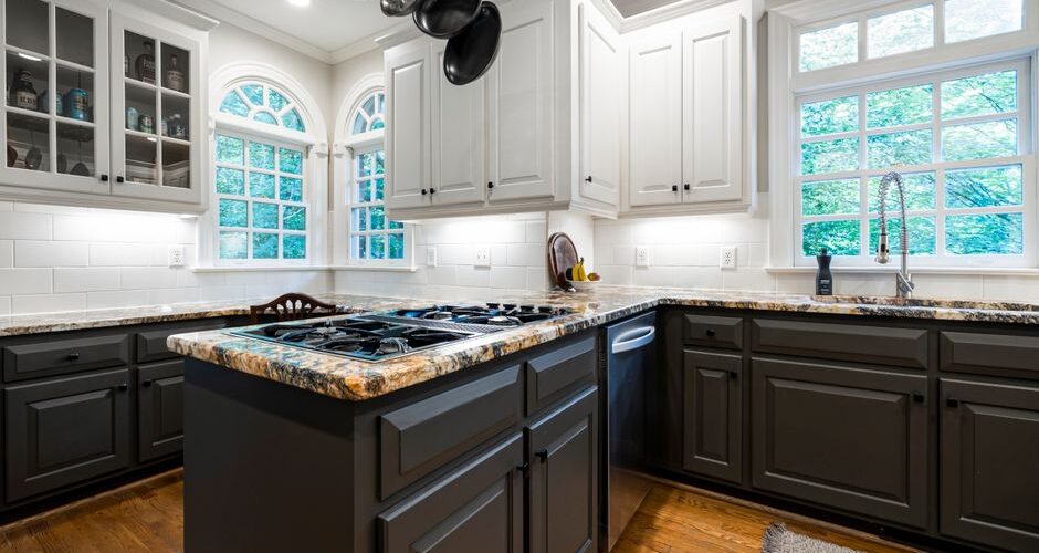 Modern kitchen with dark gray lower cabinets, white upper cabinets, a granite island with a gas stove, and a hanging pot rack.