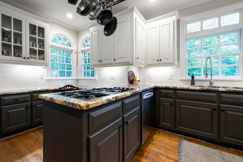 Modern kitchen with dark gray lower cabinets, white upper cabinets, a granite island with a gas stove, and a hanging pot rack.