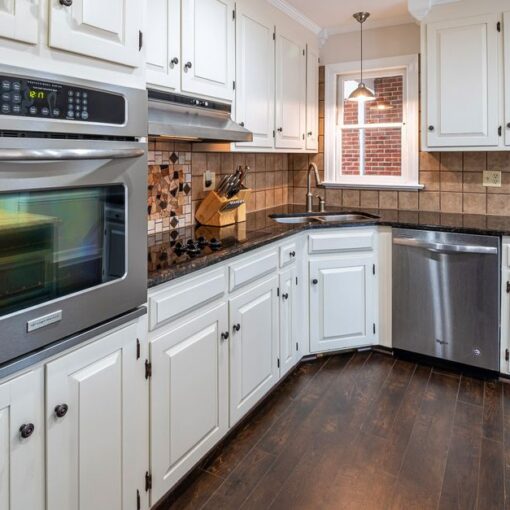 U-shaped kitchen with white cabinets, stainless steel double oven, dishwasher, and dark wood floor.
