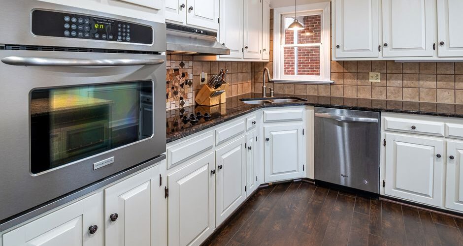 U-shaped kitchen with white cabinets, stainless steel double oven, dishwasher, and dark wood floor.