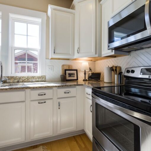 Bright, modern kitchen with white cabinets, granite counters, and stainless steel stove and microwave; double sink by windows on the left.