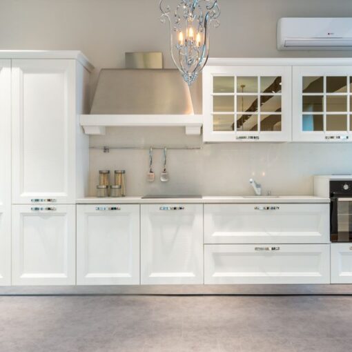 White modern kitchen with tall cabinet, stainless range hood, glass-front upper cabinets, and built-in oven.